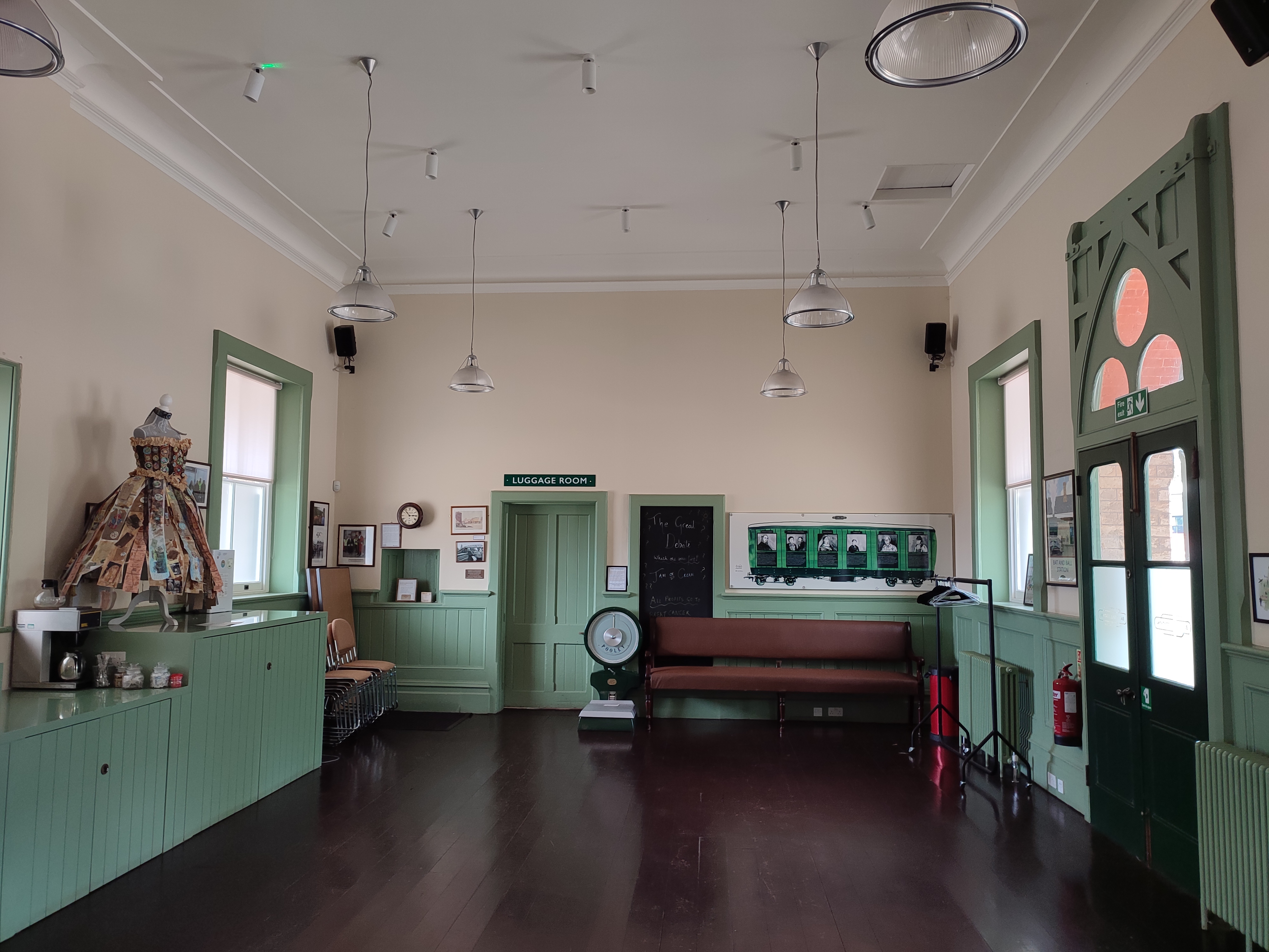 Large open hall in the station, with half green and half white walls and a wooden floor.