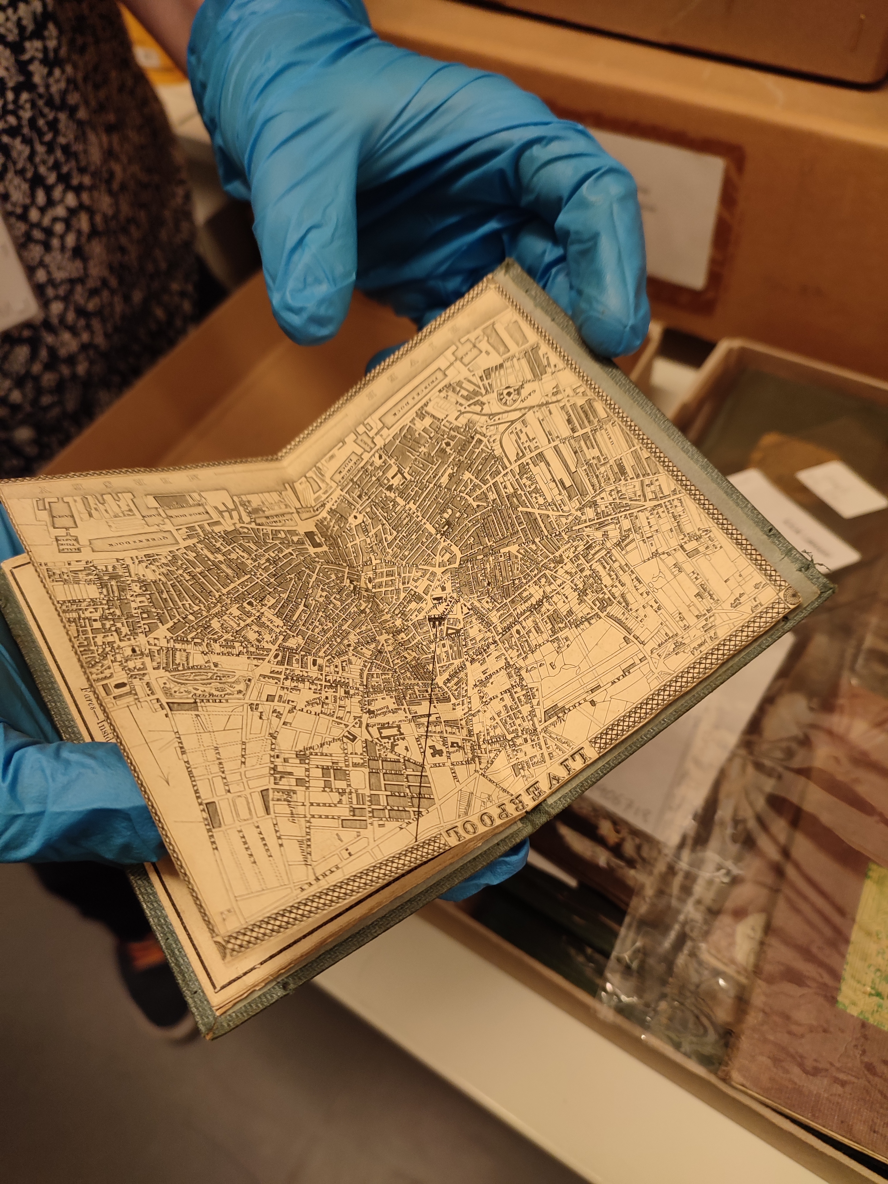 Hands with blue latex gloves, handles an old book with a detailed map .